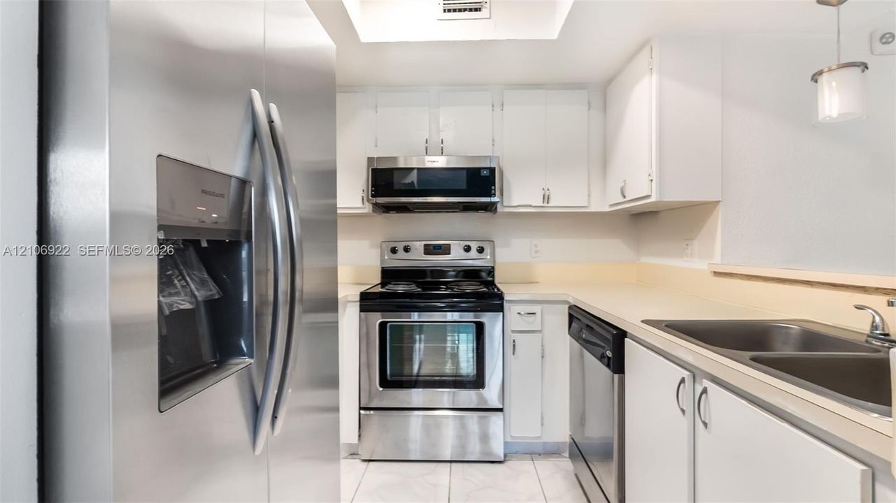 Kitchen featuring stainless steel appliances, white cabinetry, a dual-basin sink, and tile flooring