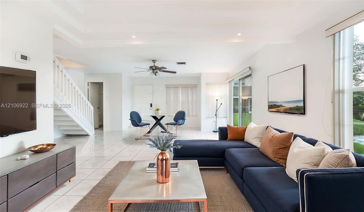 Open-concept living space featuring high tray ceilings, neutral tile flooring, a staircase with white vertical balusters, and a sliding glass door