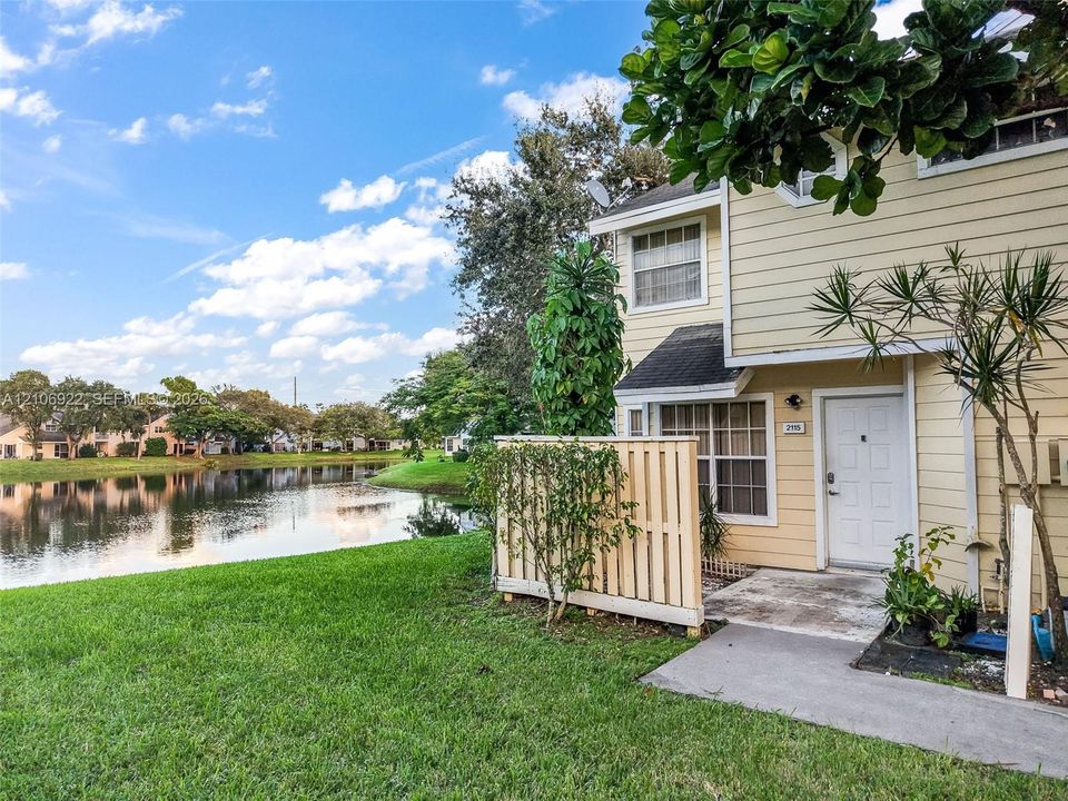 Two-story exterior with horizontal siding, covered entryway, private fenced patio area, and direct proximity to a waterfront lot