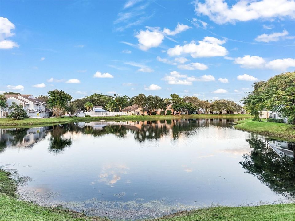 Waterfront property featuring a large pond, expansive grassy grounds, and mature trees