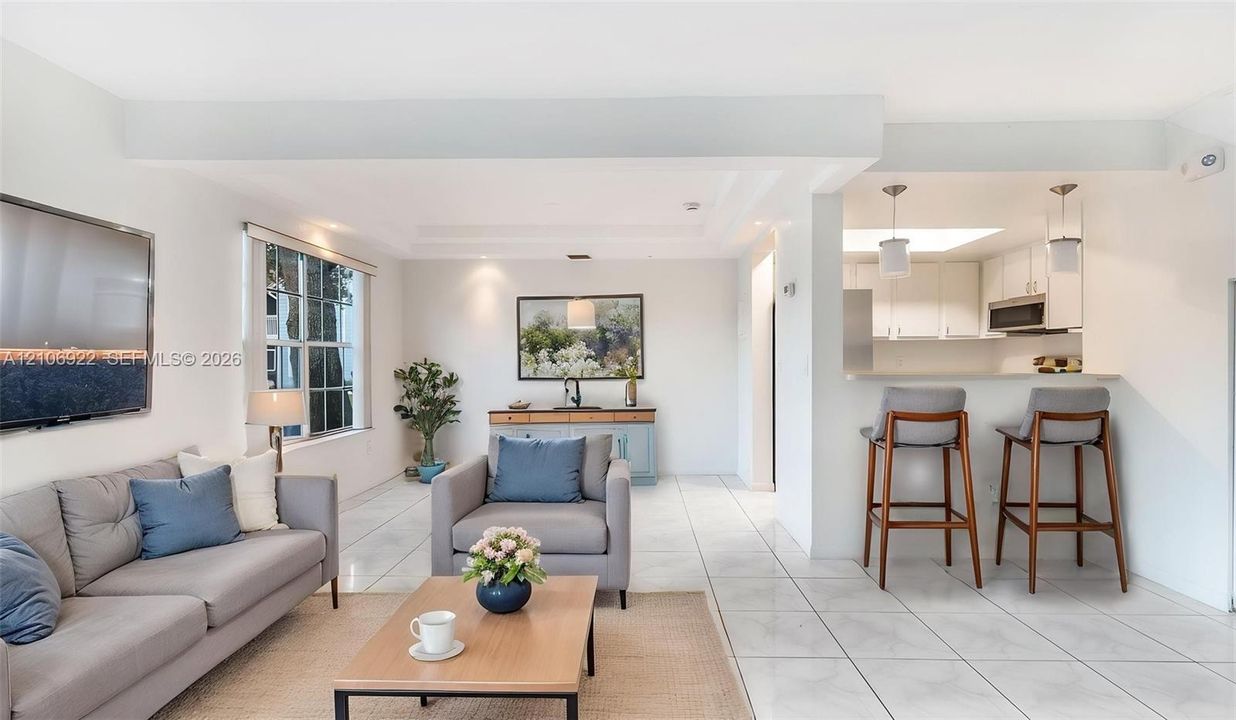 Open-concept living space featuring large-format tile flooring, a breakfast bar with dual pendant lighting, white cabinetry, and recessed ceiling lighting