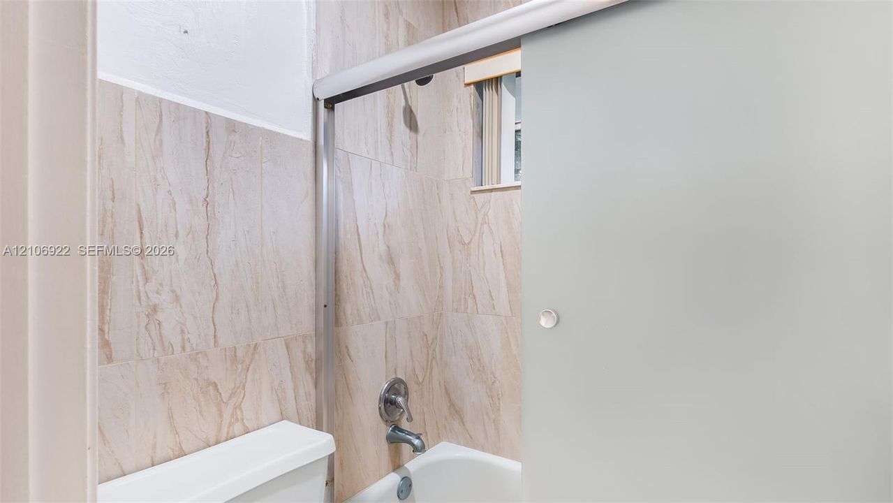 Shower area featuring full-height stone-finish tile surround, frosted glass sliding enclosure, polished chrome fixtures, and a recessed window