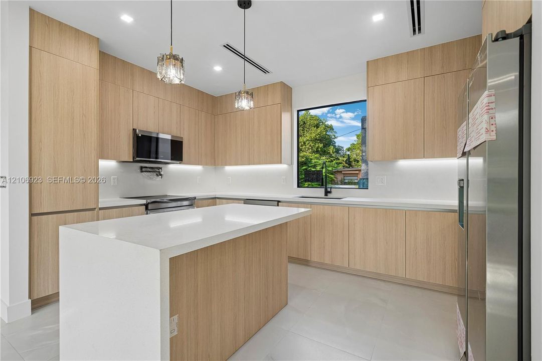 Kitchen featuring flat-panel wood-finish cabinetry, a waterfall-edge island, white countertops, recessed lighting, and stainless steel appliances