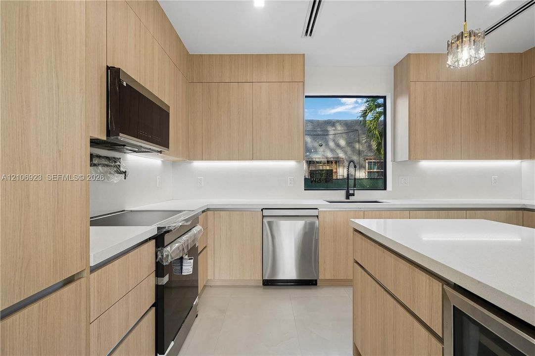 Kitchen featuring flat-panel wood-finish cabinetry, white solid-surface countertops, an integrated center island, stainless steel appliances, and under-cabinet lighting