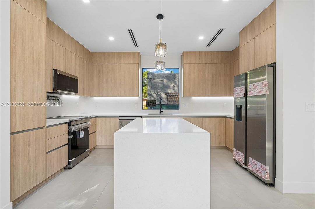 Modern kitchen featuring flat-panel wood-finish cabinetry, a large quartz-topped island, stainless steel appliances, under-cabinet lighting, and recessed ceiling lighting