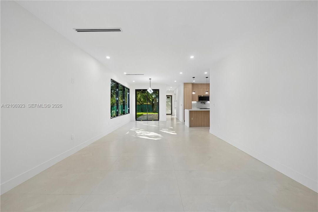 Open floor plan featuring large-format tile flooring, recessed lighting, expansive glass sliding doors, and a kitchen equipped with natural wood-finish cabinetry