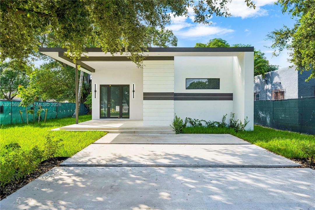 Modern exterior featuring smooth white stucco finish, flat roofline with dark trim, expansive concrete driveway, covered porch, and vertical wall-mounted lighting fixtures