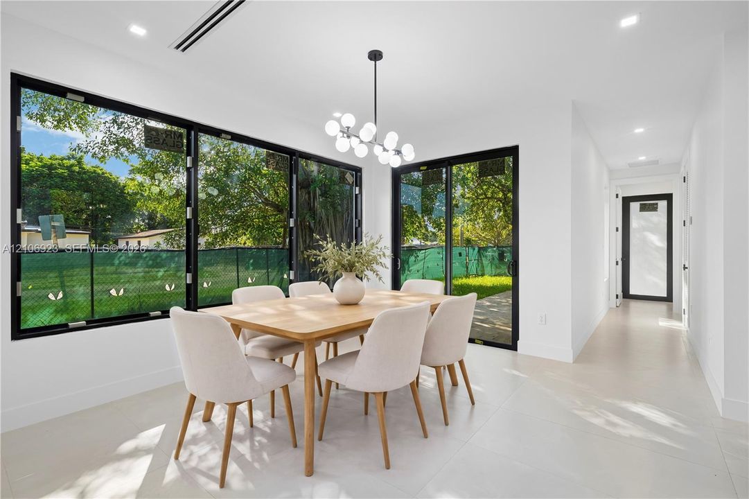 Dining area featuring expansive floor-to-ceiling black-framed windows, integrated recessed lighting, a modern multi-globe chandelier, and porcelain tile flooring