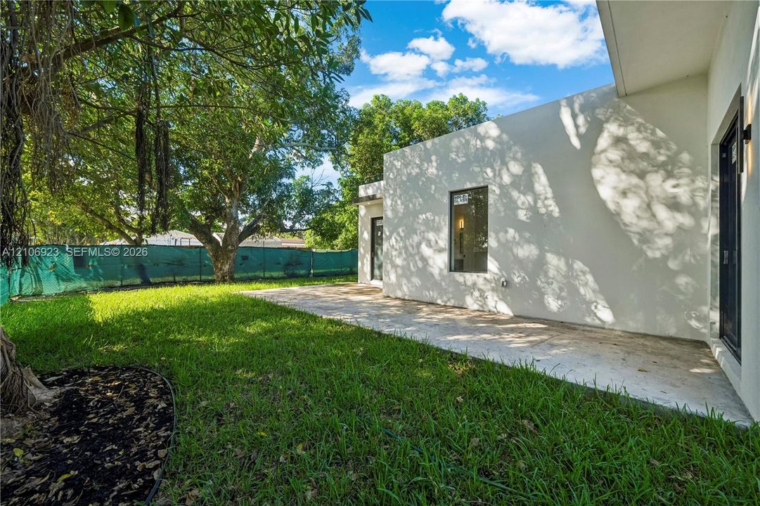 Backyard featuring a paved patio, manicured lawn, mature trees, and an exterior light fixture