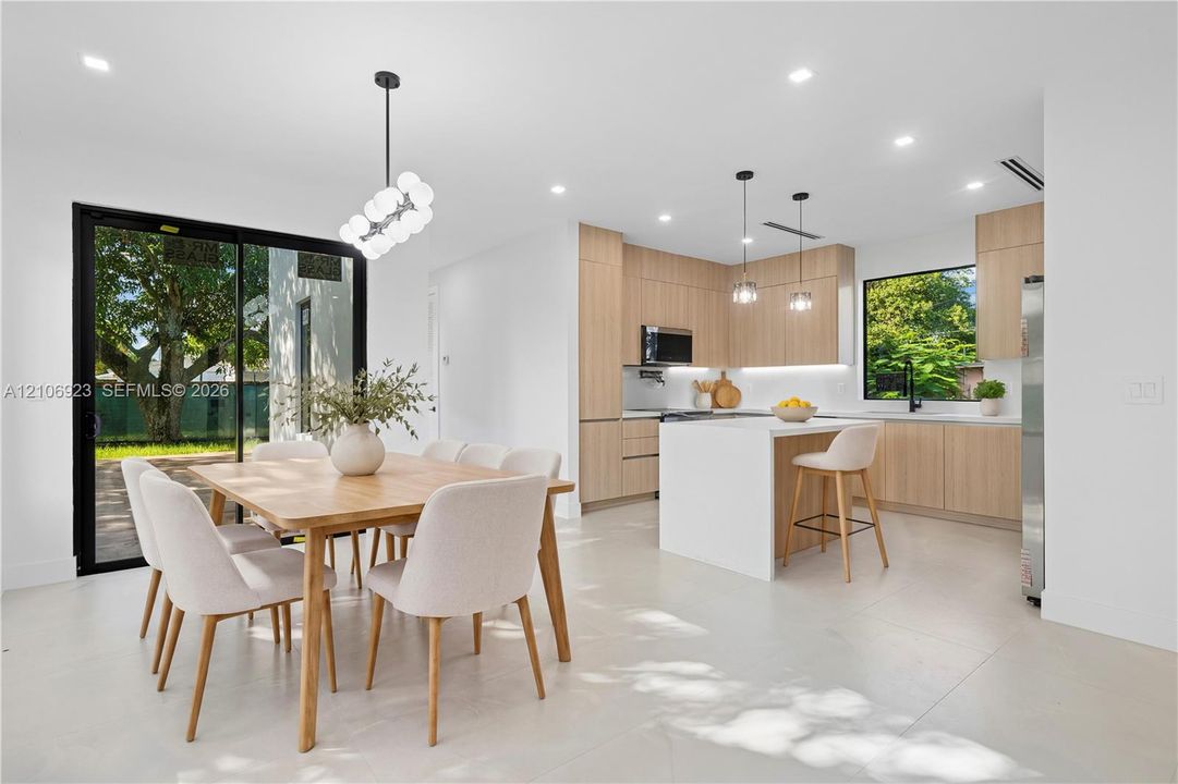 Modern kitchen featuring flat-panel wood cabinetry, a waterfall-edge center island with quartz countertops, recessed lighting, and large sliding glass doors providing outdoor access