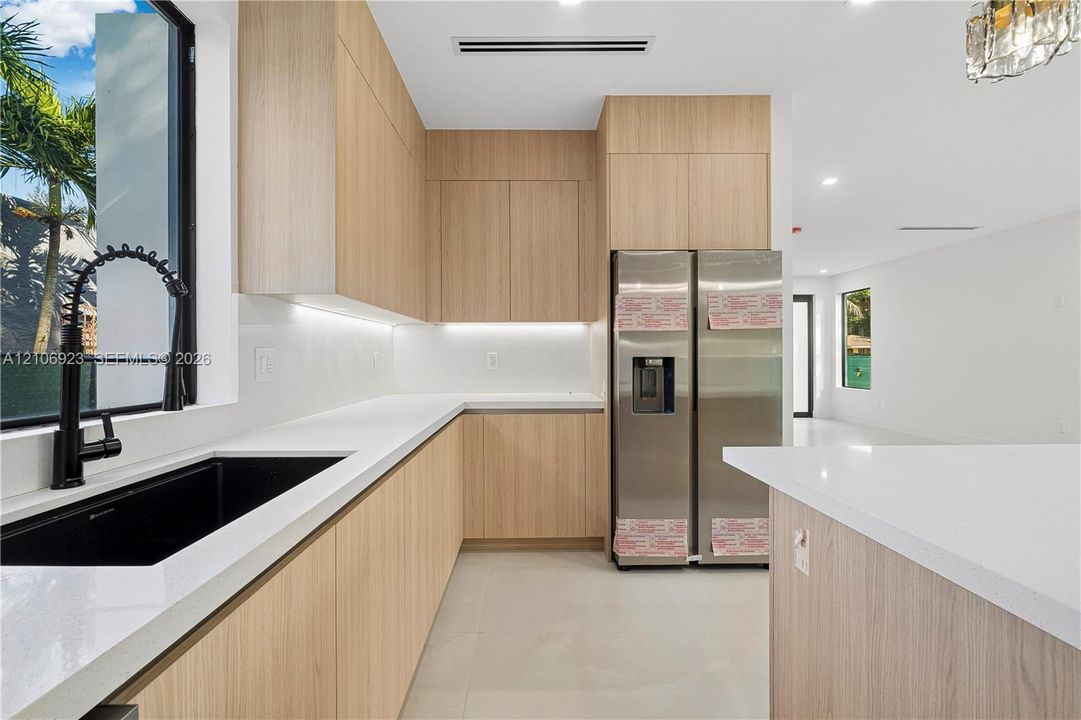 Kitchen featuring flat-panel wood-finish cabinetry, white countertops, black undermount sink with high-arc faucet, stainless steel refrigerator, and recessed lighting