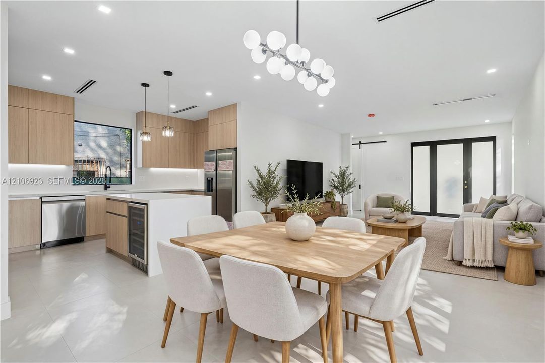 Open-concept kitchen featuring light wood-finish cabinetry, a central island with an integrated beverage cooler, stainless steel appliances, and a modern multi-globe chandelier