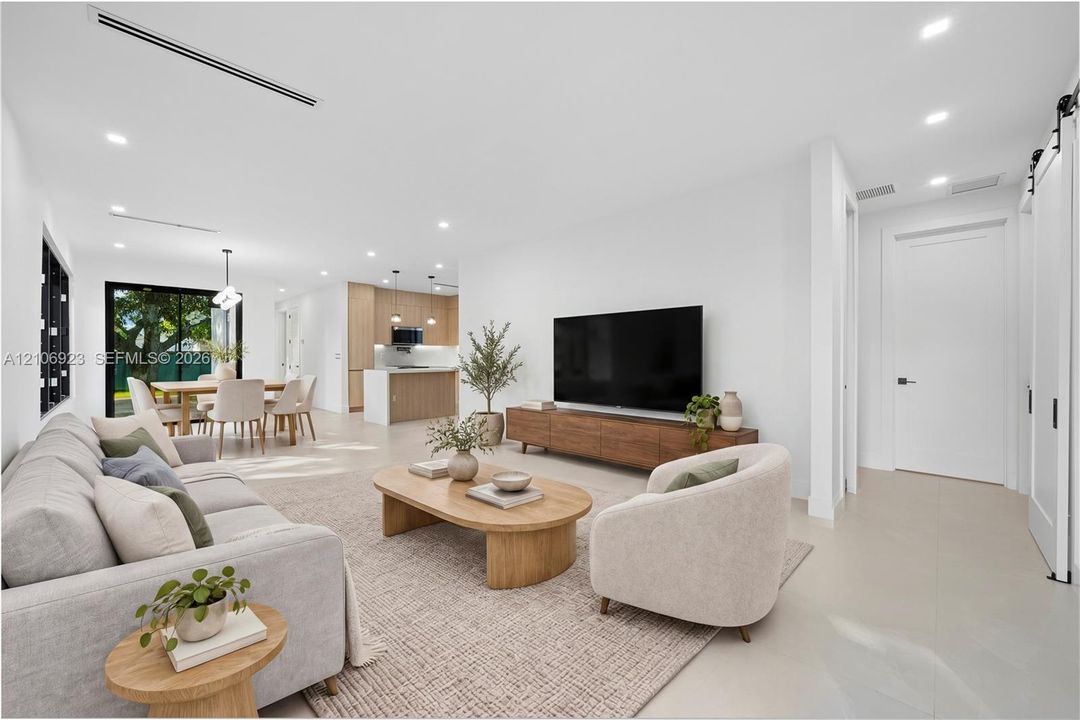 Open-concept interior featuring light-toned flooring, recessed lighting, linear HVAC diffusers, white sliding barn door, and kitchen cabinetry with wood-finish accents