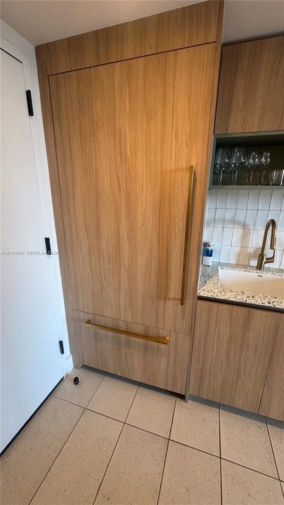 Panel-ready built-in refrigerator with wood-finish cabinetry, metallic hardware, speckled stone-finish countertop, white tile backsplash, and a gold-tone gooseneck faucet