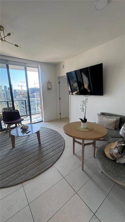 Floor-to-ceiling glass windows, neutral tile flooring, and metallic chandelier lighting