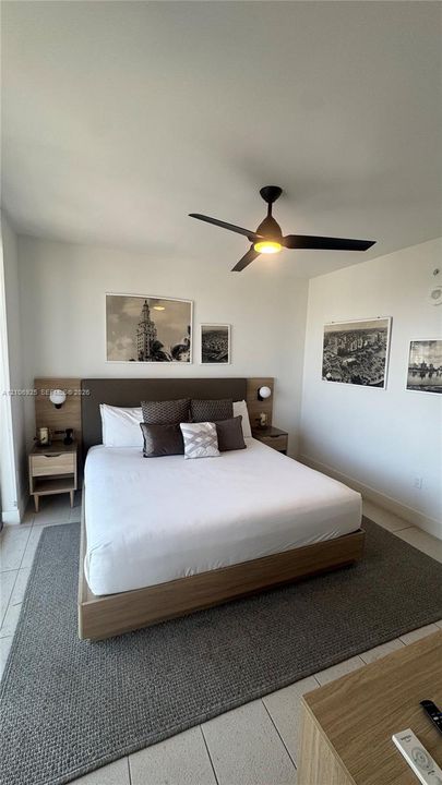 Integrated headboard with wood-finish paneling and wall-mounted spherical light fixtures, complemented by a modern ceiling fan and large-format tile flooring
