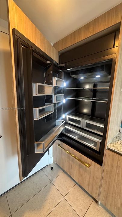 Panel-ready built-in refrigerator featuring wood-finish cabinetry, metallic hardware, glass shelving, and integrated lighting