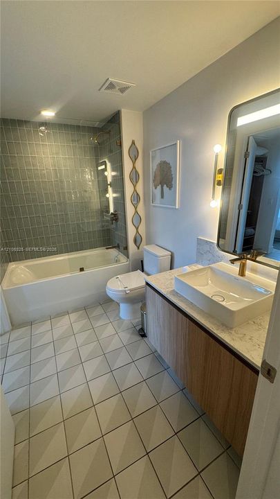 Bathroom featuring a wood-finish vanity with a stone-top vessel sink, matte gold faucet, geometric floor tile, and a glass-enclosed shower with vertical wall tile