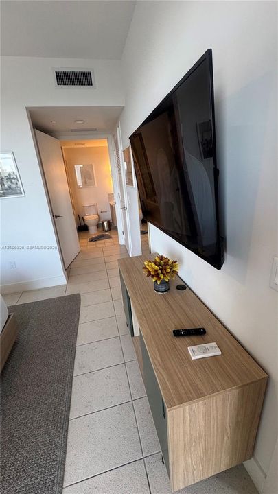 Wall-mounted flat-screen display, custom floating console with wood-finish cabinetry, and neutral tile flooring