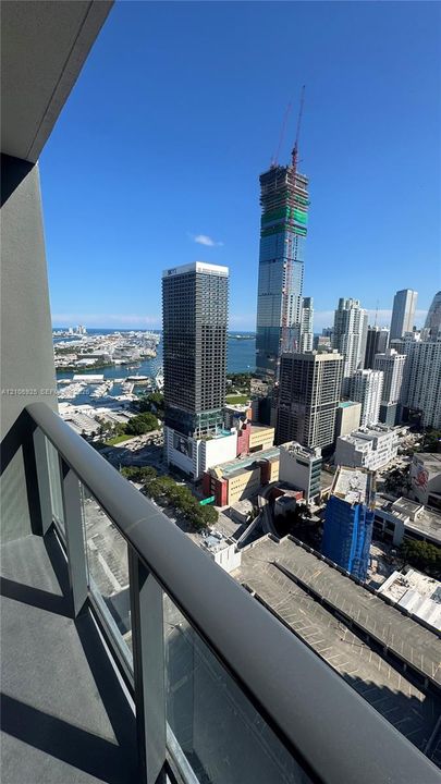 Covered balcony with a glass and metal railing featuring panoramic urban and waterfront scenery