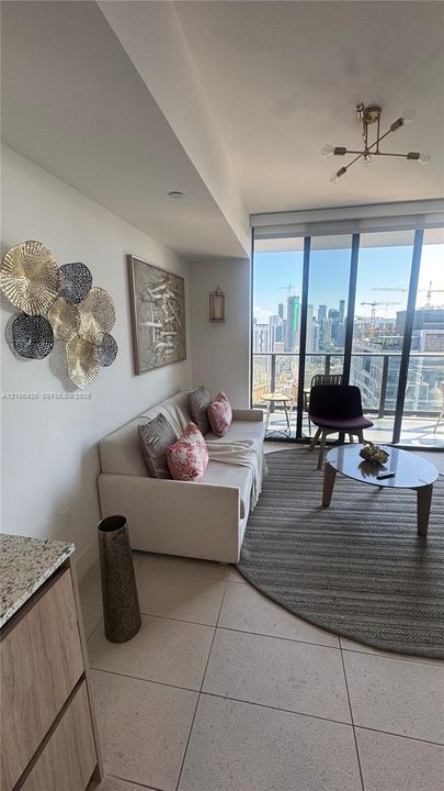 Floor-to-ceiling windows, porcelain tile flooring, modern multi-arm light fixture, and an attached balcony