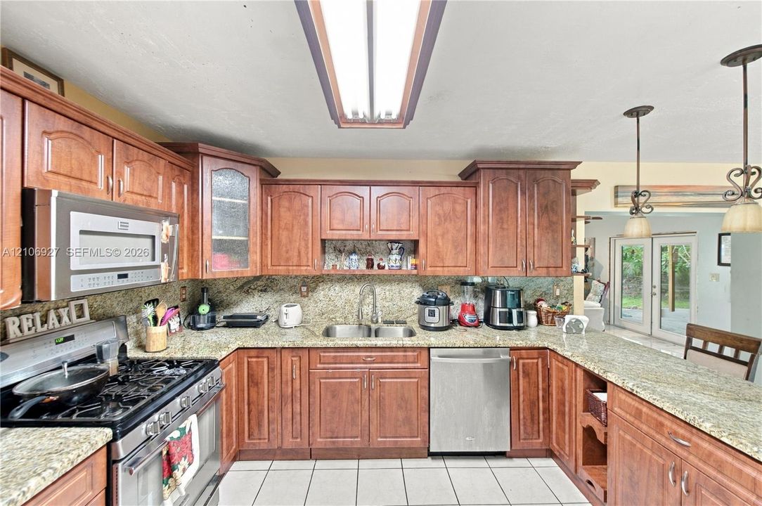 Kitchen featuring stained wood cabinetry, stone-surface countertops, stainless steel appliances including a gas range and built-in microwave, dual-basin under-mount sink, and ceramic tile flooring
