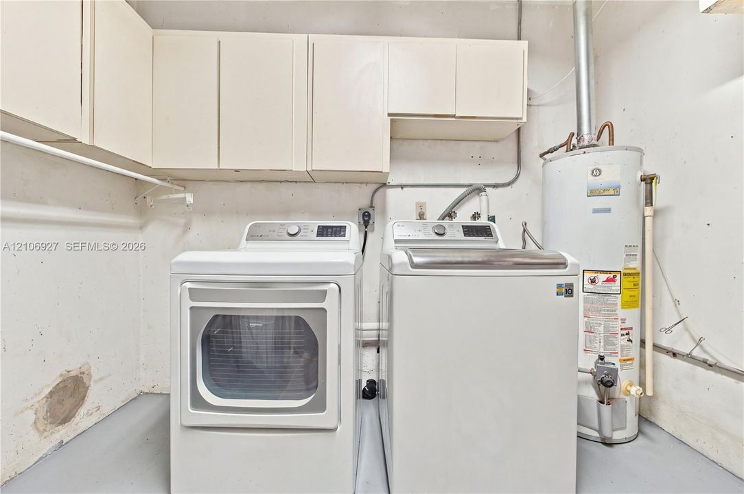 Utility space featuring white overhead cabinetry, dedicated washer and dryer connections, and a water heater
