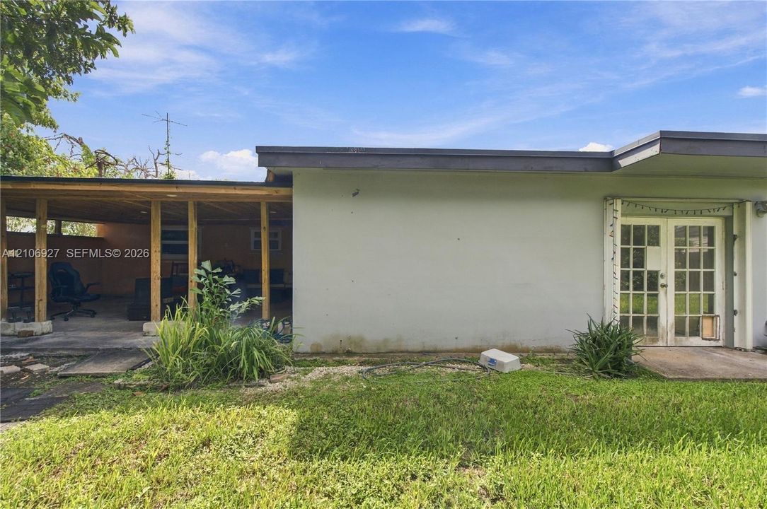 Exterior elevation featuring a covered patio with exposed wood framing, smooth stucco siding, and full-glass French doors