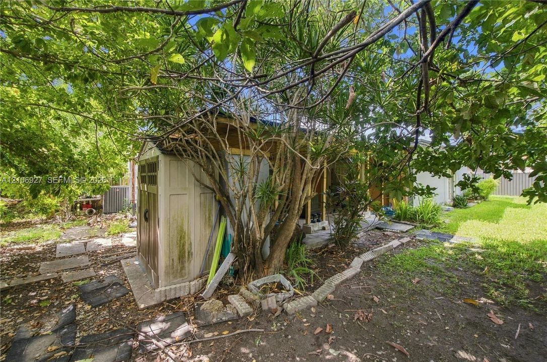 Backyard featuring mature trees, lawn area, stone paver accents, and a storage structure