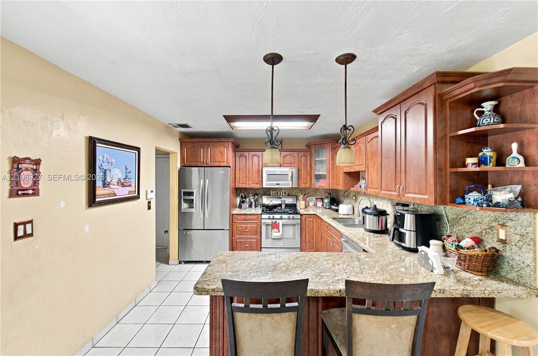 Kitchen featuring wood cabinetry, stone countertops, stainless steel appliances, tile flooring, and pendant lighting