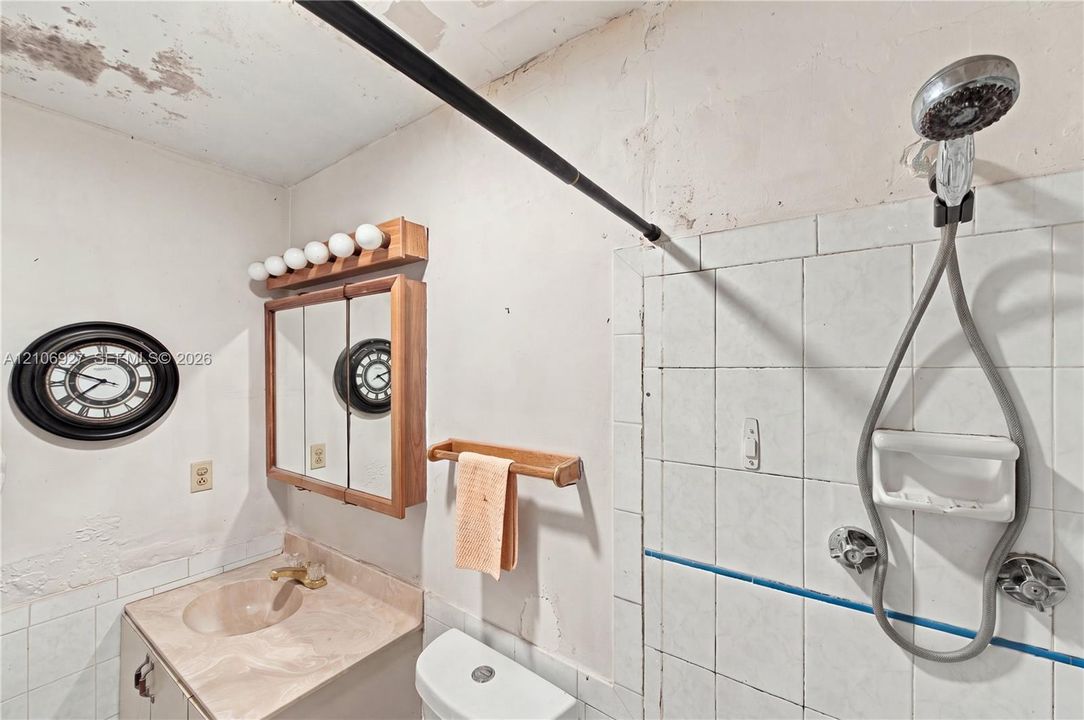 Bathroom featuring a vanity with an integrated sink, a multi-bulb light fixture, a mirrored medicine cabinet, a tiled shower surround, and a wall-mounted showerhead