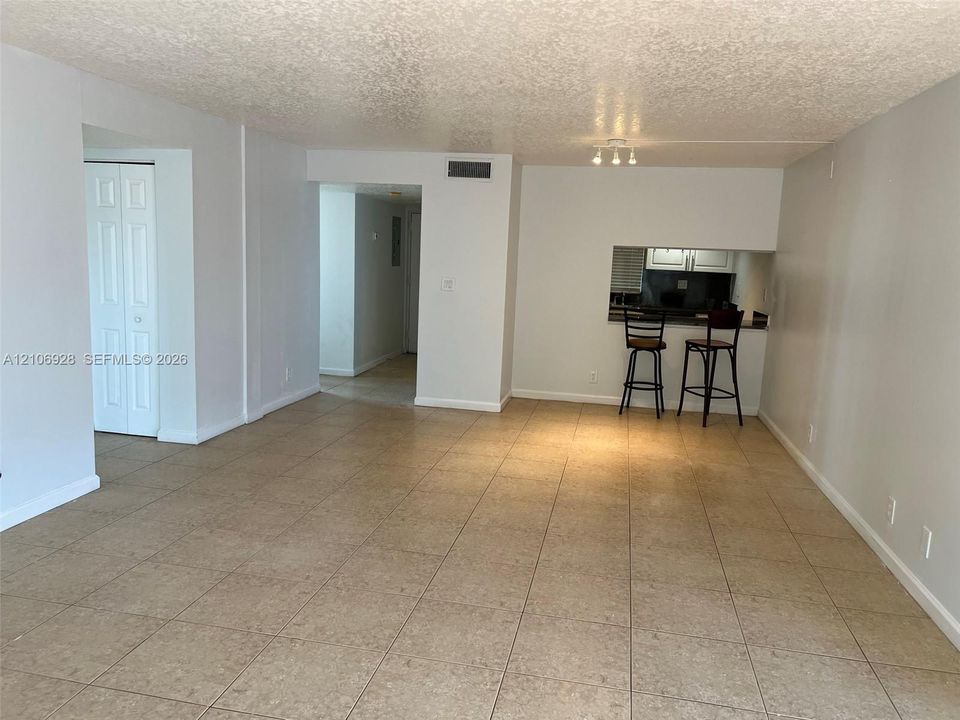 Open-concept interior featuring neutral wall tones, large-format tile flooring, a pass-through opening, and dual-panel closet doors