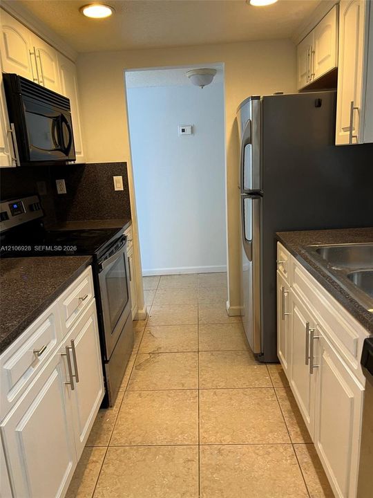 Kitchen featuring white cabinetry with brushed metal hardware, dark stone-finish countertops, stainless steel appliances, and tile flooring