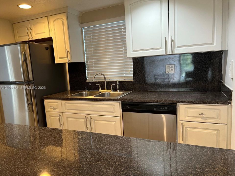 Kitchen featuring white cabinetry, dark stone-finish countertops, stainless steel appliances, dual-basin stainless steel sink, and recessed lighting