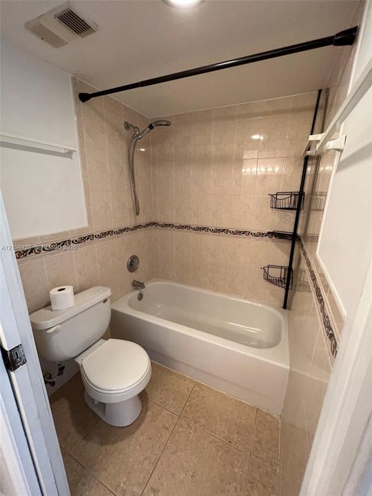 Bathroom featuring a tub-shower combination, neutral tiled walls with decorative accents, ceramic tile flooring, and a standard toilet