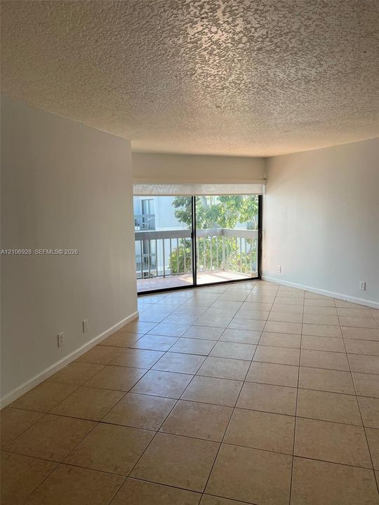 Living area featuring large-format tile flooring, textured ceilings, and a sliding glass door providing access to a private balcony