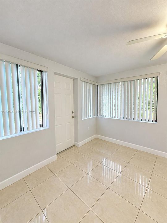 Neutral-toned tile flooring, multiple windows with vertical blinds, and a ceiling fan