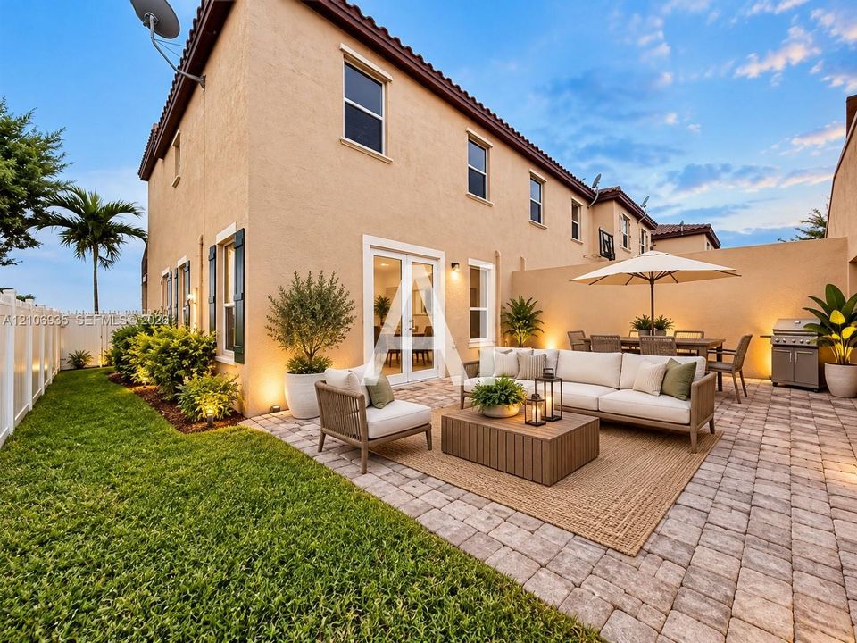 Stucco exterior featuring a paver patio, integrated perimeter masonry wall, white vinyl fencing, and a manicured lawn