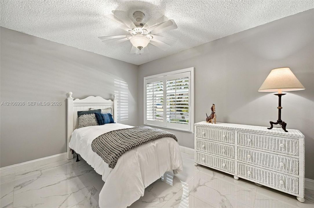 Room featuring large-format stone-finish tile flooring, ceiling fan with integrated lighting, and white plantation shutters