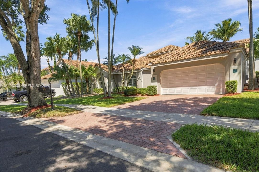 Stucco exterior featuring a multi-hipped tile roof, attached two-car garage, and a decorative paver driveway