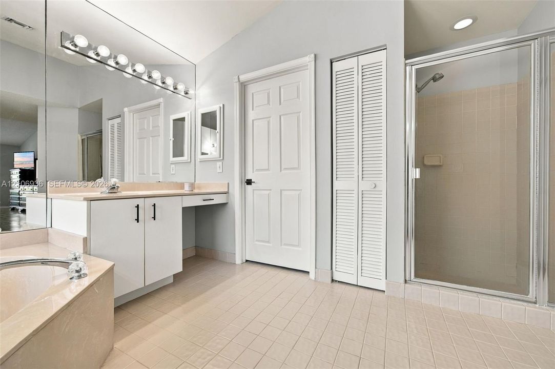 Bathroom featuring a tiled floor, walk-in shower with a glass enclosure, built-in vanity with a sit-down counter, and an expansive wall-mounted mirror with integrated light fixtures