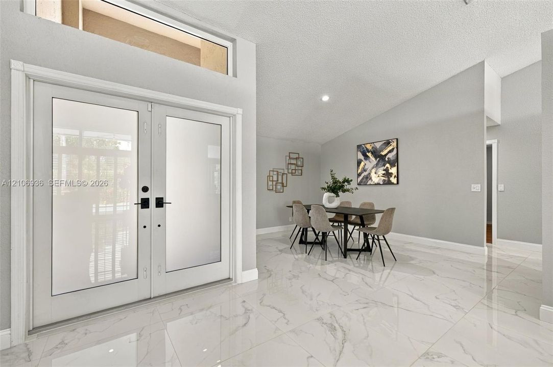 Double-door entry with frosted glass inserts, polished large-format tile flooring, vaulted ceilings, and a rectangular transom window