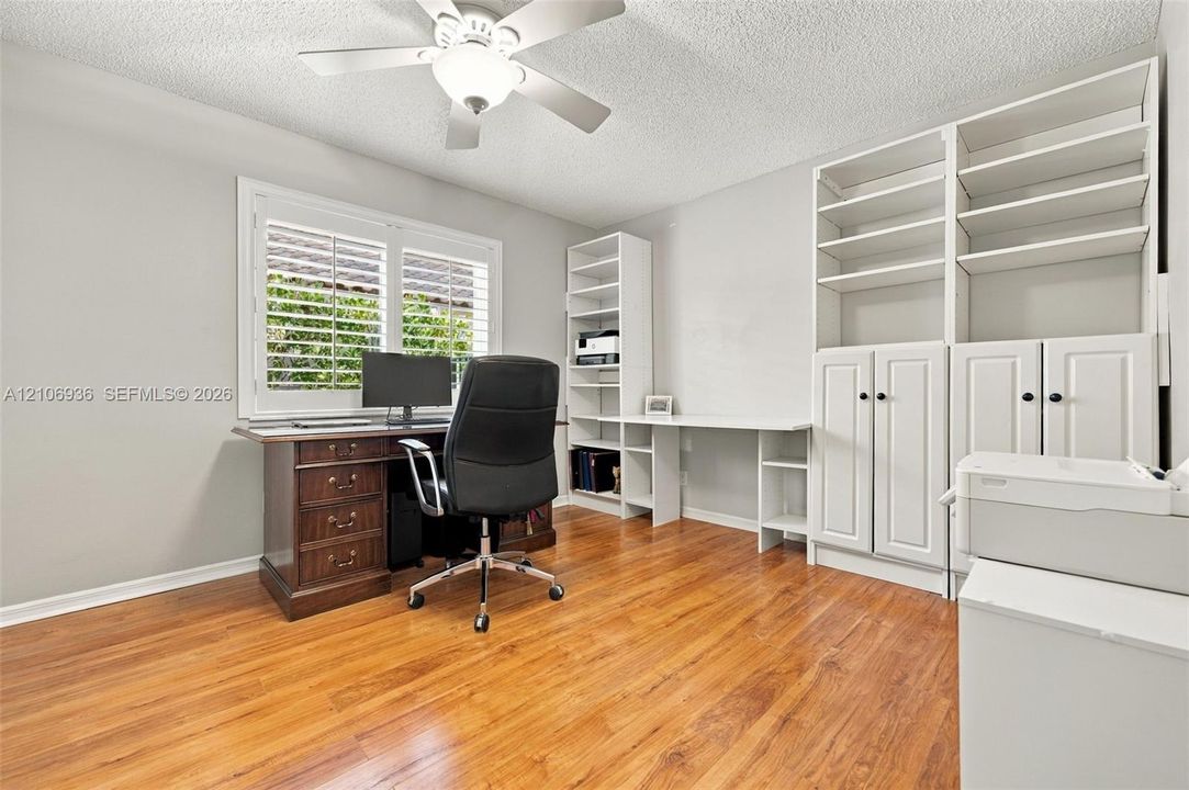 Custom built-in white cabinetry with open shelving and workspace, wood-finish flooring, and white plantation shutters