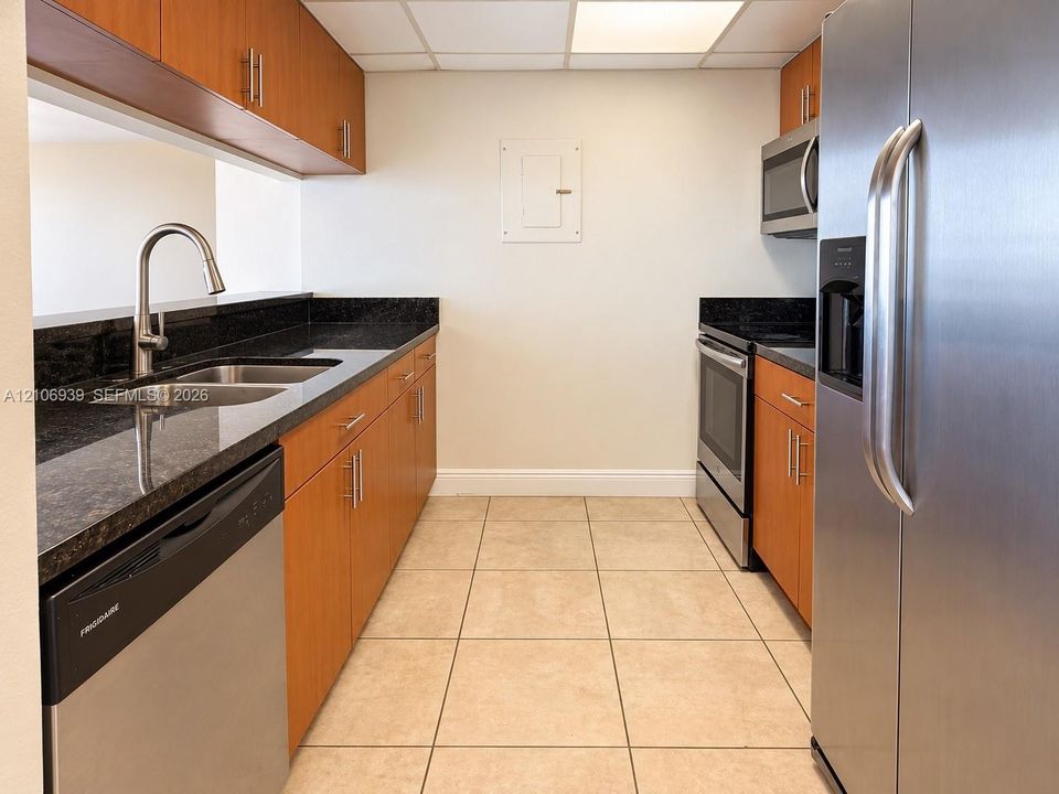 Kitchen featuring wood-finish cabinetry, dark stone countertops, stainless steel appliances, ceramic tile flooring, and an undermount dual-basin sink with a pull-down faucet