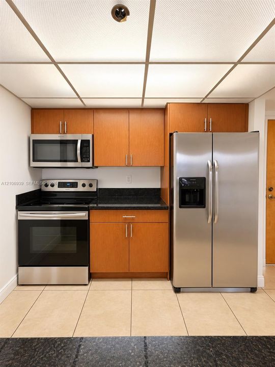 Kitchen featuring flat-panel wood-finish cabinetry, dark solid-surface countertops, stainless steel appliances, and large-format tile flooring