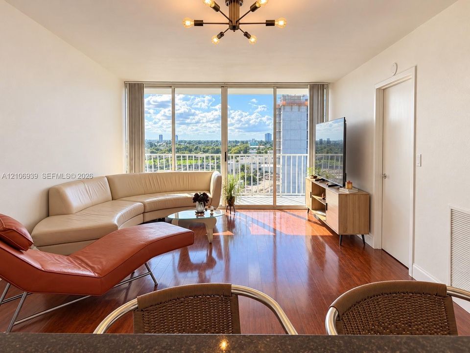 Wood-finish flooring, floor-to-ceiling glass sliding doors, private balcony, and multi-arm geometric ceiling fixture