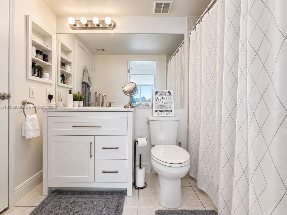 Bathroom featuring a white vanity cabinet with stone countertop, undermount sink, brushed nickel hardware, and built-in recessed wall shelving