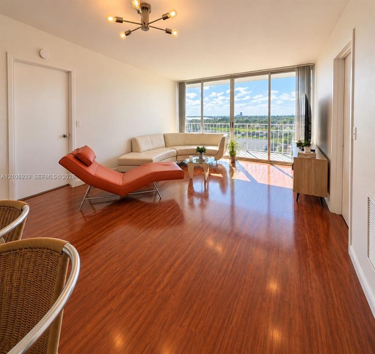 Living area featuring wood-finish flooring, floor-to-ceiling sliding glass doors, a balcony, and a multi-arm modern light fixture