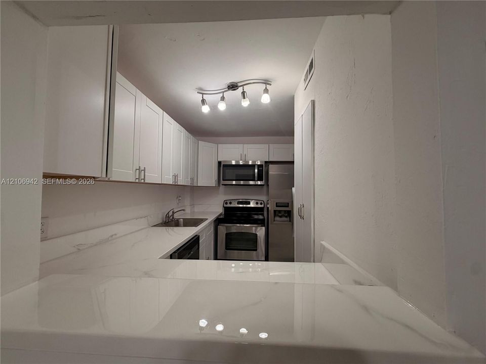 Kitchen featuring white shaker-style cabinetry, stone-finish countertops, stainless steel appliances, and multi-light track lighting