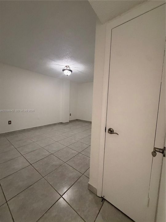 Neutral-toned tile flooring, flush-mount ceiling lighting, and a solid-core interior door with metallic hardware